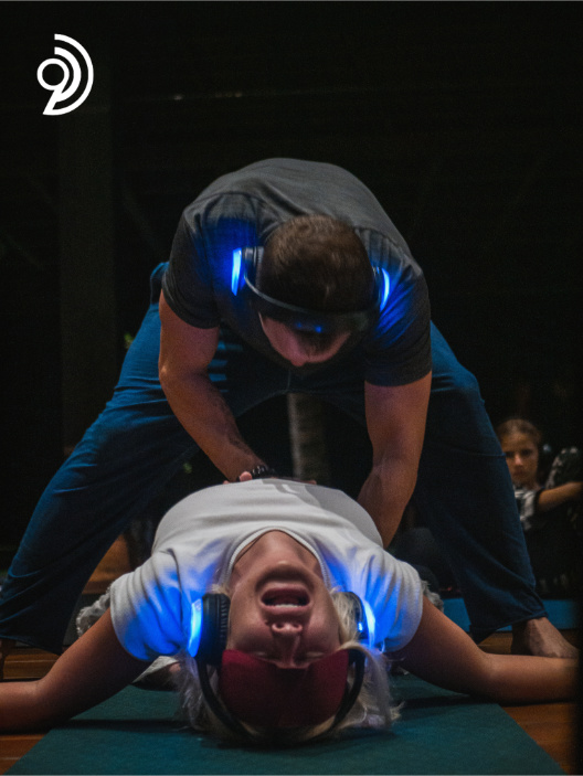 9D Breathwork Session image, from Breathwork Coach in Barrie, showing someone standing over top of another person who has there back arched and are wearing an eye covering and headphones
