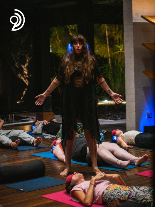 9D Breathwork Session image, from Breathwork Coach in Barrie, where someone is standing in the room with their eyes closed and a headset on while others are laying on the floor on mats with their eyes covered and headsets on