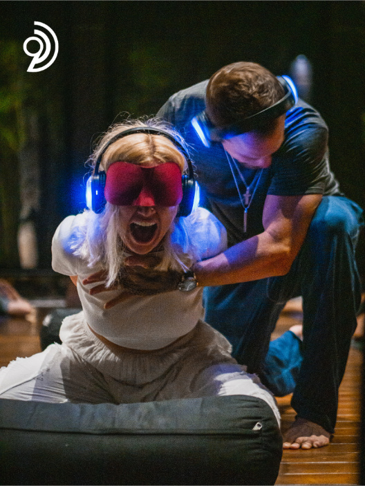 9D Breathwork Session image, from Breathwork Coach in Barrie, with someone crouched holding on to someone who is sitting with their eyes covered and a headset on and they are screaming