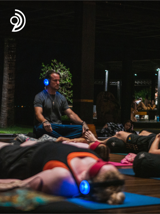 9D Breathwork Session image, from Breathwork Coach in Barrie, with someone sitting with their eyes closed and a headset on while others lay on the floor around them with their eyes covered and a headset on